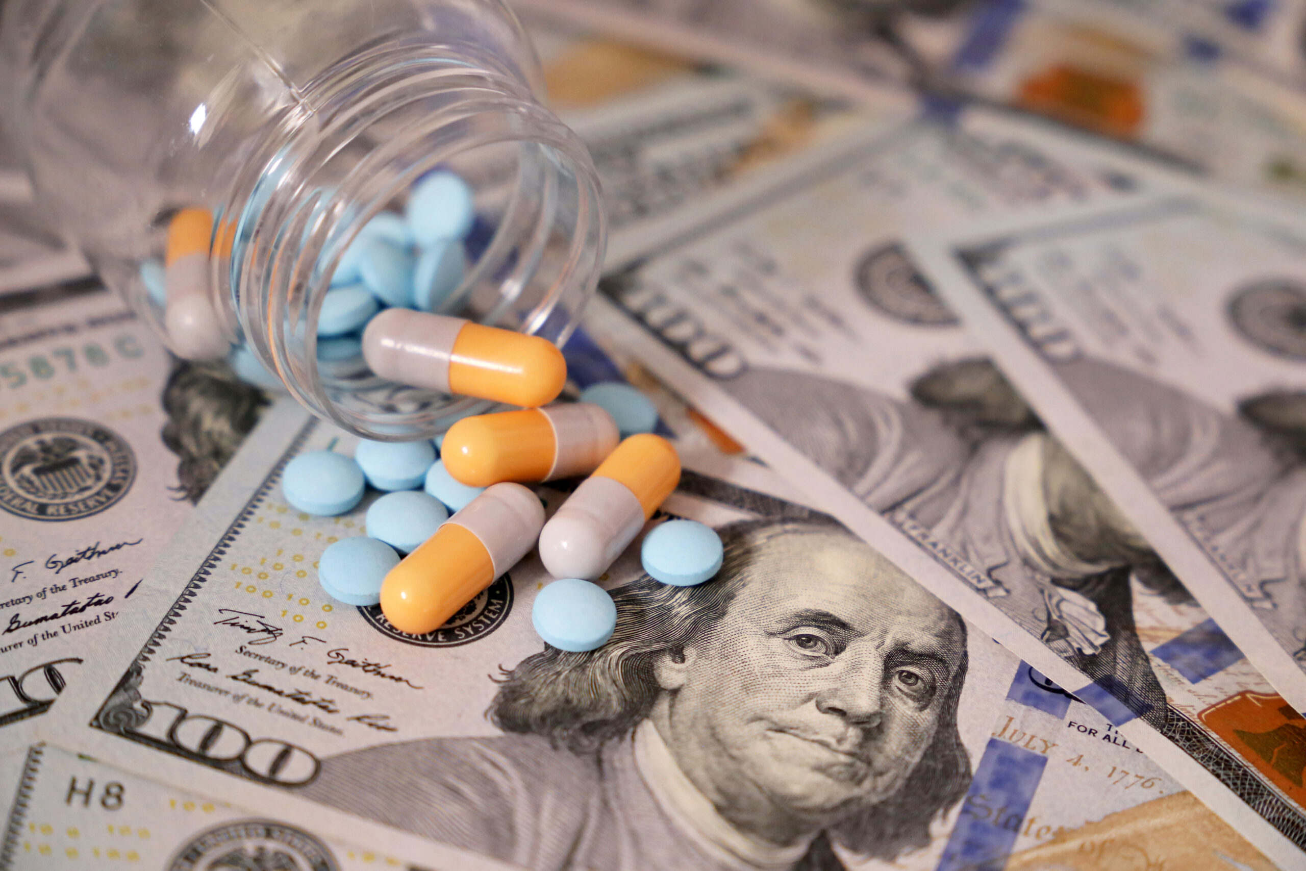 Pills and capsules in a bottle on US dollars bills. Representing the rising drug costs