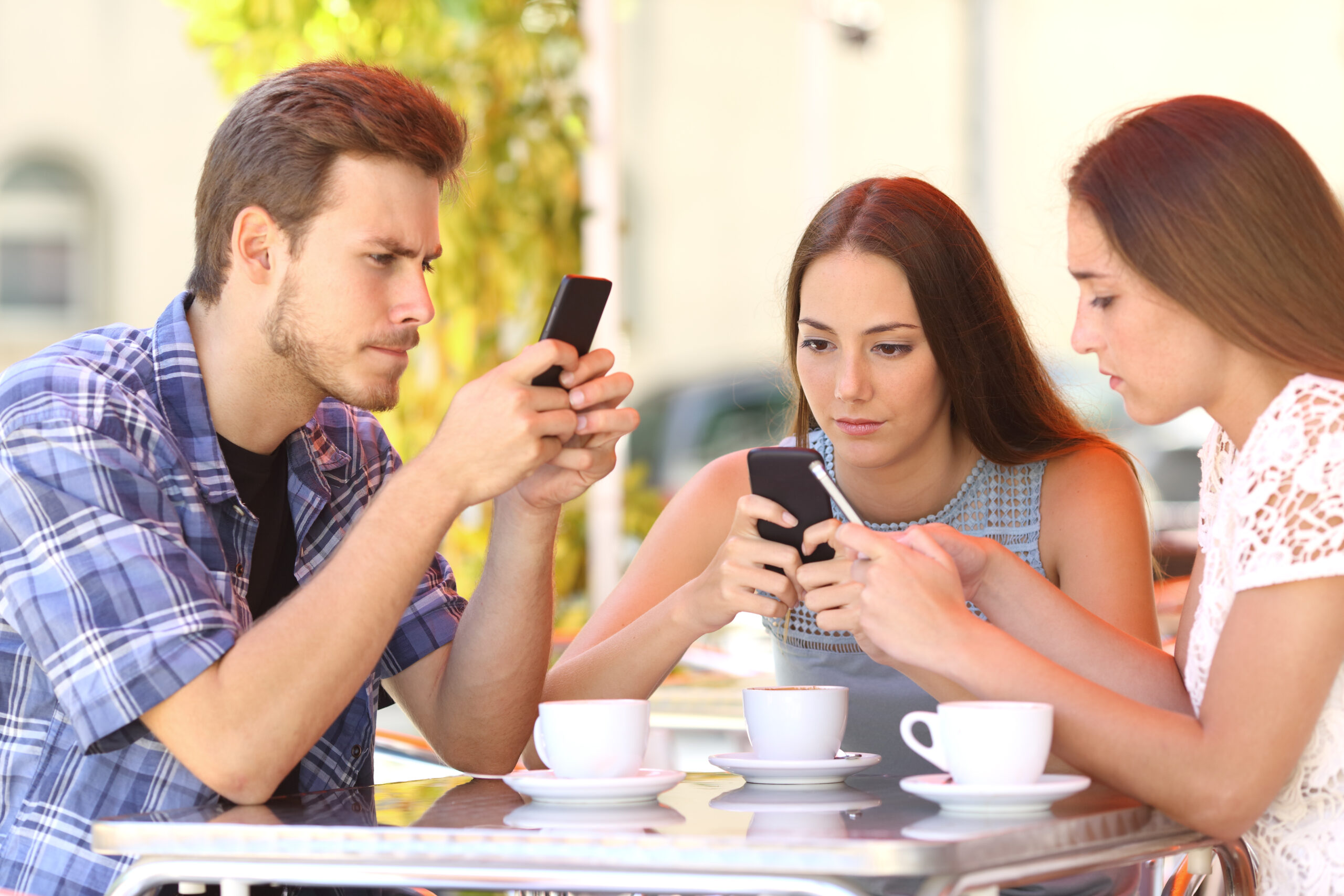 Group of three smart phone addicted friends in a coffee shop terrace everyone with one cellphone