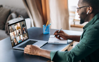 An African-American male engaging with peers via video conference call while doing remote work.