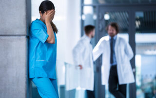 Nurse experiencing stress while two doctors converse in the background.