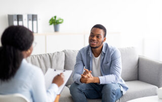 Young African-American male talking to his psychologist, receiving professional help at mental health clinic.