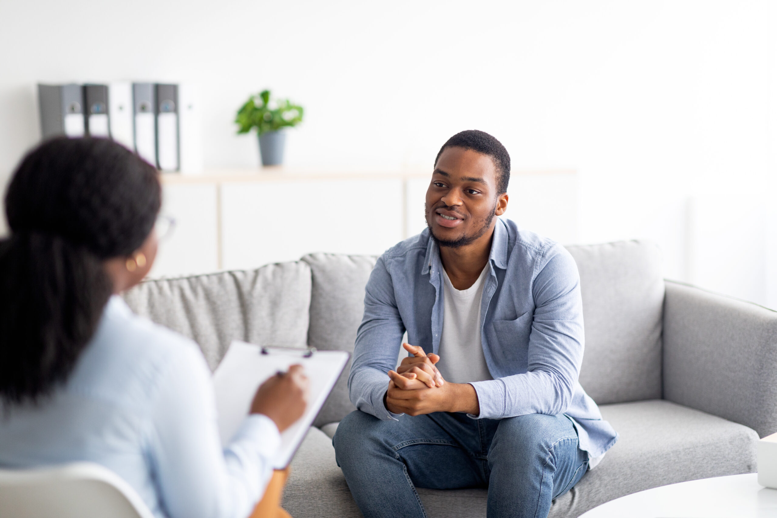 Young African-American male talking to his psychologist, receiving professional help at mental health clinic.