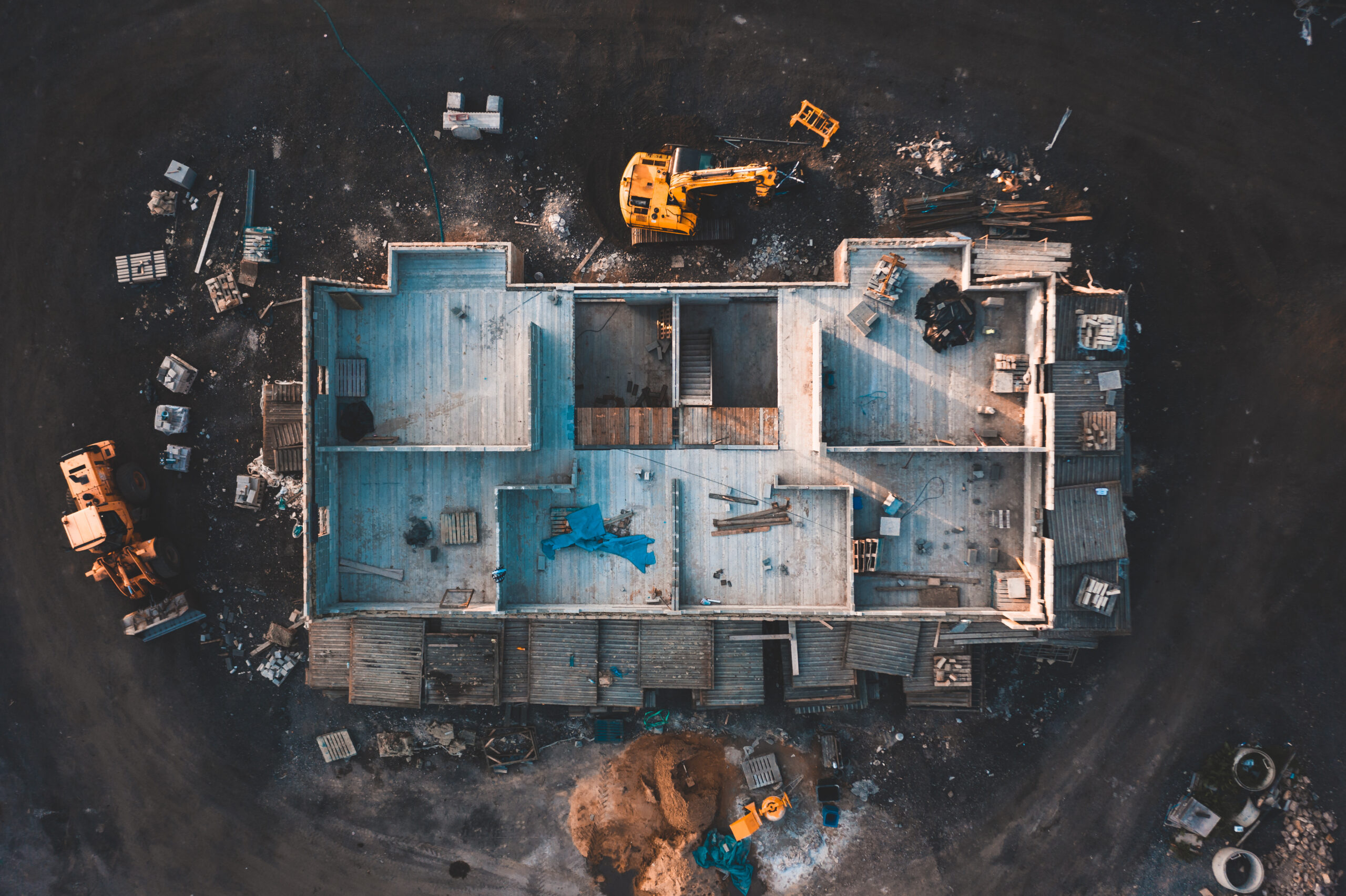 Aerial birds eye image of the frame of a house being built on a construction site at sunset - Wooden floor and walls are visible. Several attractive nuisances are visible