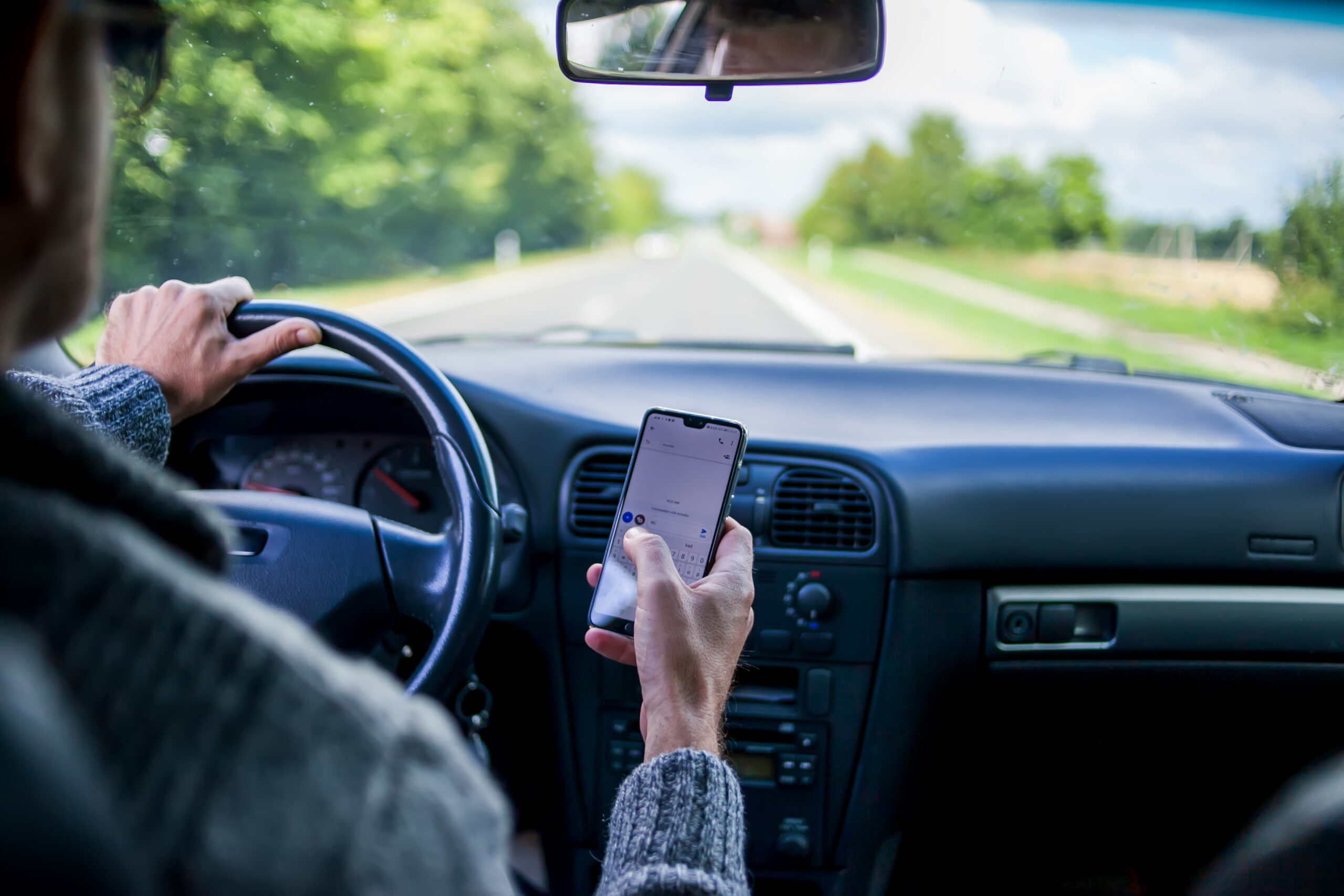 A man is using a cell phone doing what is considered distracted driving.