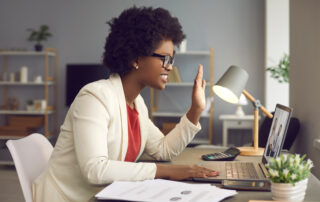 Side view of business woman waving in front of webcam greeting via video link.