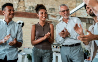 Employee Satisfaction: Multicultural team clapping their hands and smiling while standing in the creative office. Celebrating success