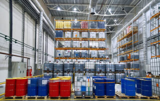 Chemical Storage: Oil drums and plastic container on pallets in a warehouse on metal shelving. Handling and storing industrial lubricants.