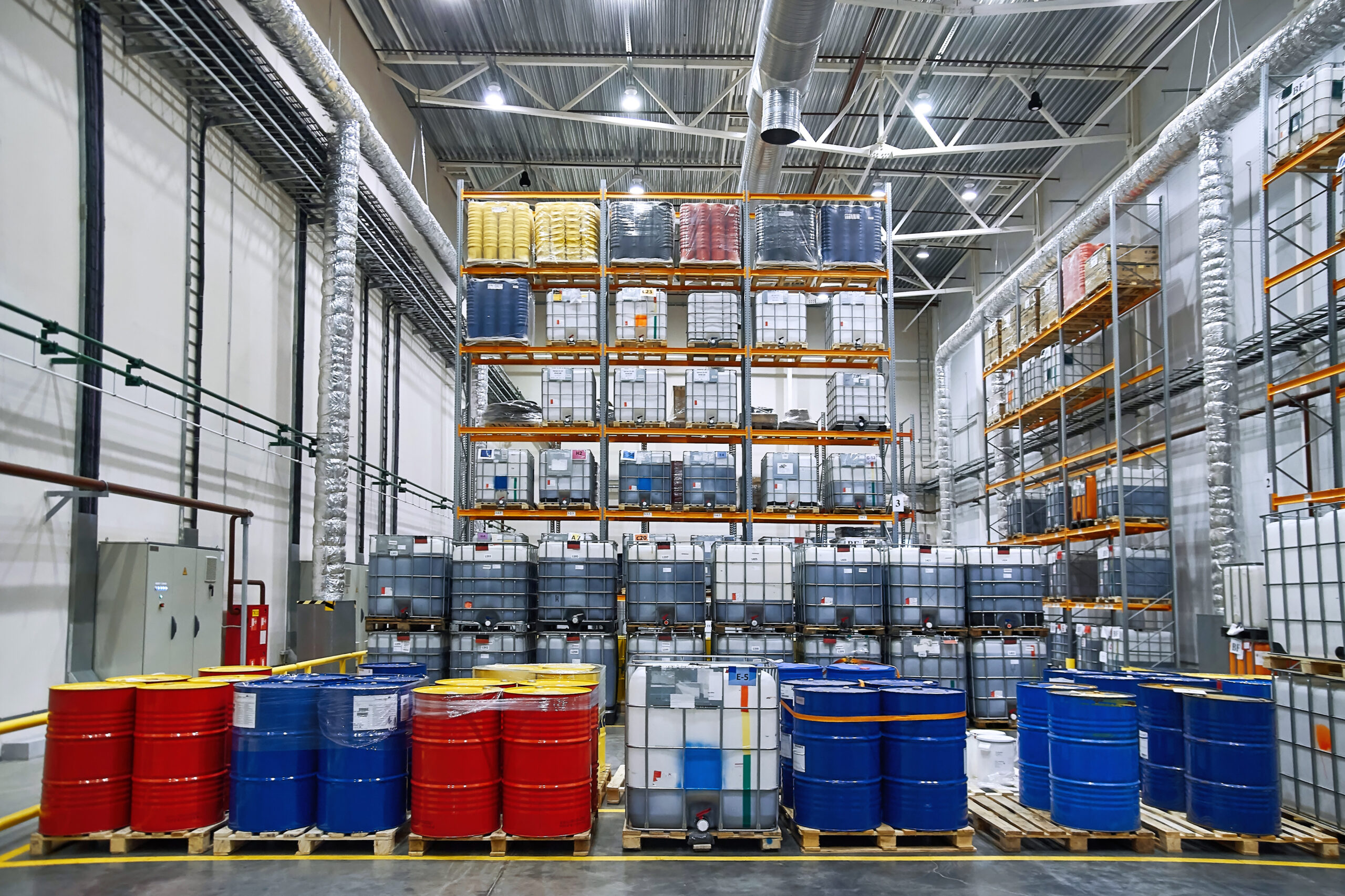 Chemical Storage: Oil drums and plastic container on pallets in a warehouse on metal shelving. Handling and storing industrial lubricants.