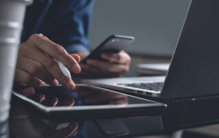 Multitasking business man using digital tablet and mobile smart phone, busy working on laptop computer in modern office. Software developer, apps designer testing mobile application on smartphone, close up