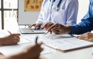Team, medical analysts and doctors consulting with paperwork of graphs, data and charts in hospital conference room.