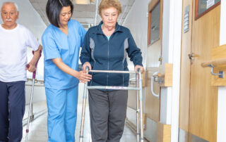 patient transfers: doctor helping elder woman with walker and man in hospital aisle.