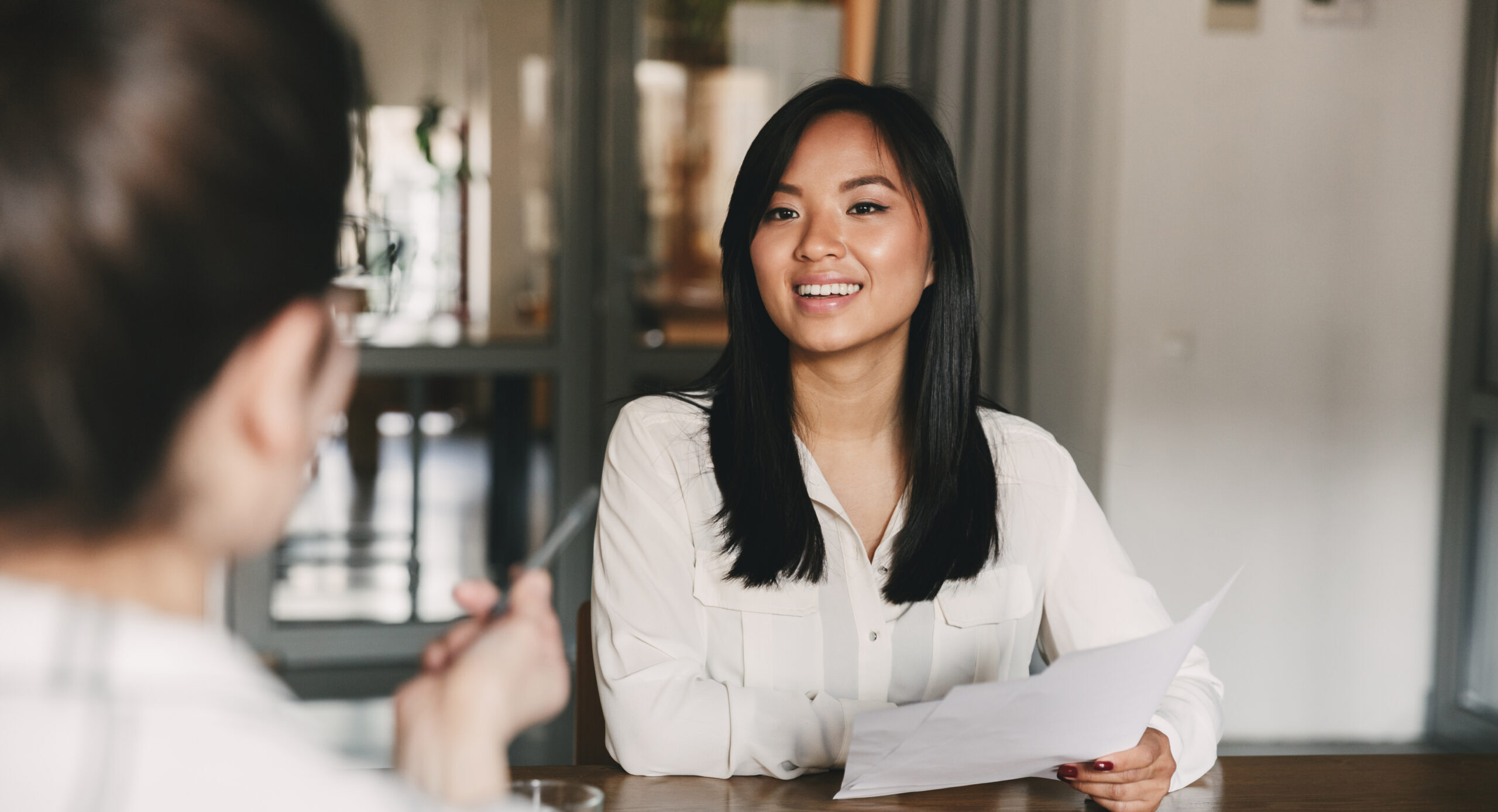 Business, career and placement concept - joyful asian woman smiling and holding resume while sitting in front of directors during corporate meeting or job interview