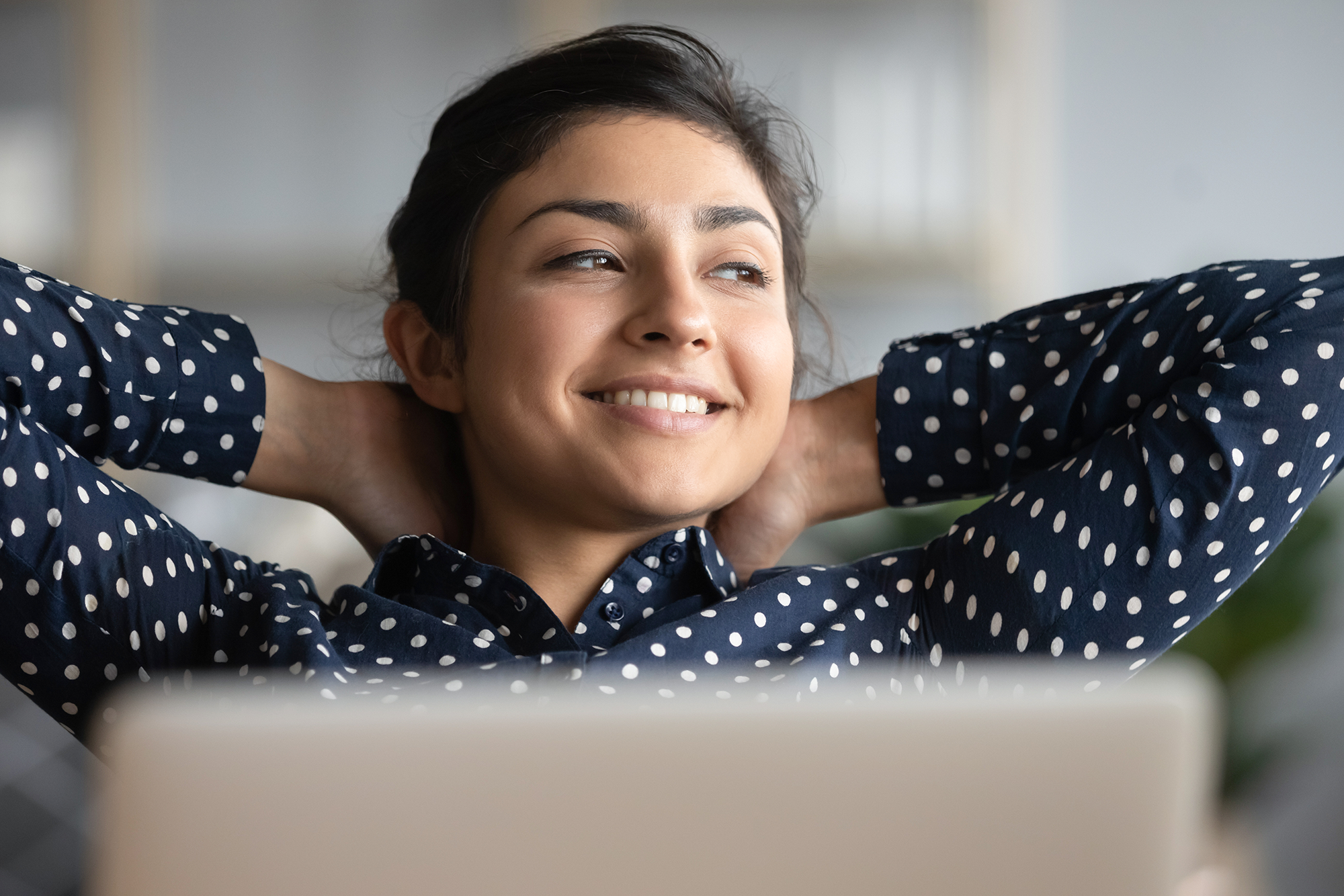 Improving Employee Satisfaction by Moving Beyond Workplace Flexibility and Hybrid Schedules: woman sitting at her desk, relaxing.