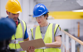 A department lead going over paperwork with a fellow construction colleague. The review of return-to-work policies help prevent medical mismanagement.