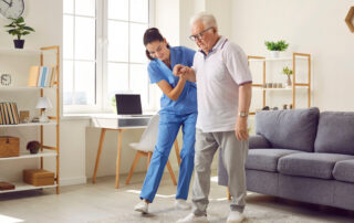 Avoiding Slips trips and falls: Young nurse helping elderly man walk in the room, holding his hand, supporting him. Treatment and rehabilitation after injury or stroke, life in assisted living facility, senior care concept