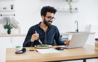 Rethink Your Healthcare Offerings: a man sitting at his desk, eating a salad while working remotely.