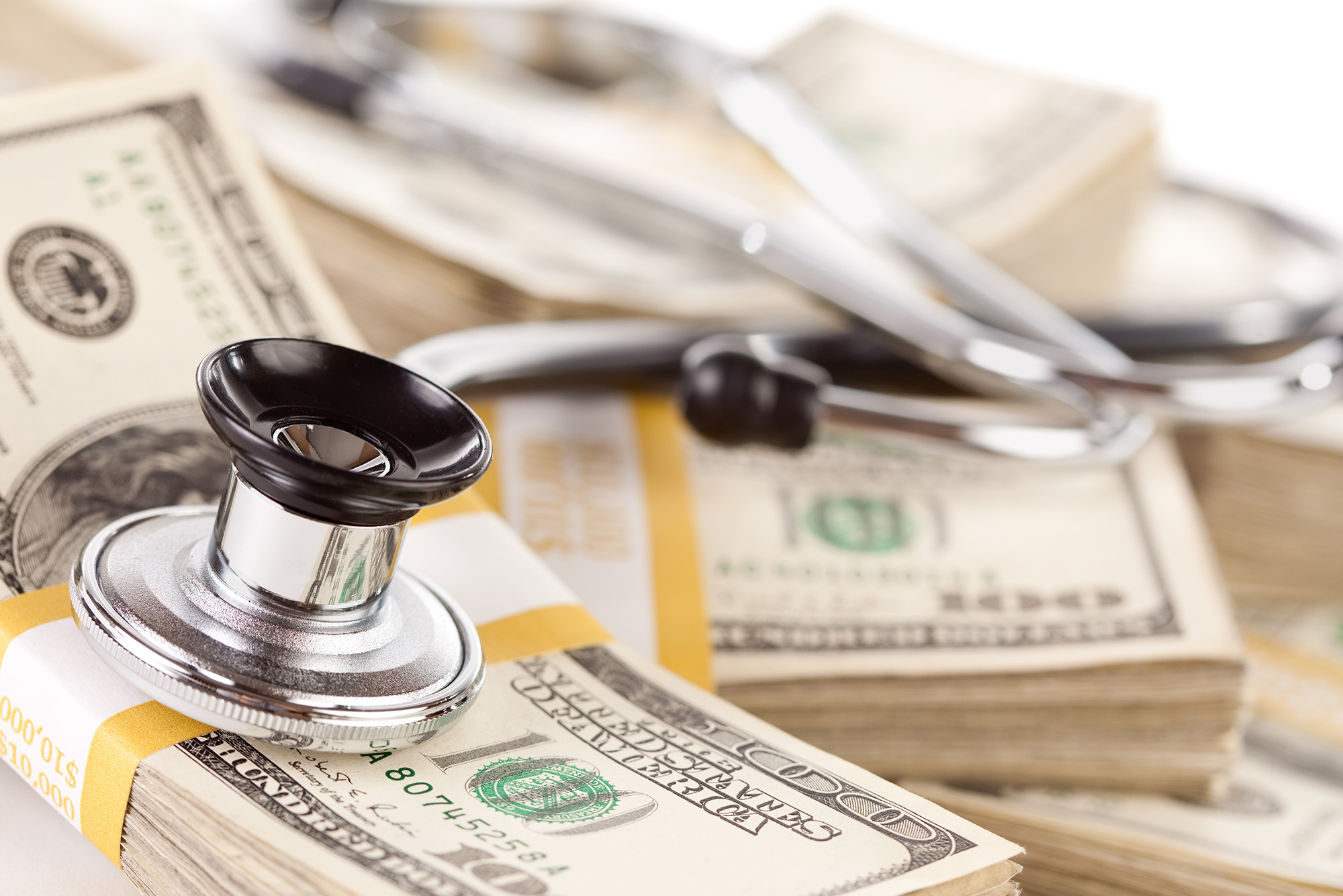 Healthcare Spending Expected to Exceed Overall Economic Growth: a stethoscope sitting on a stack of $100 bills.