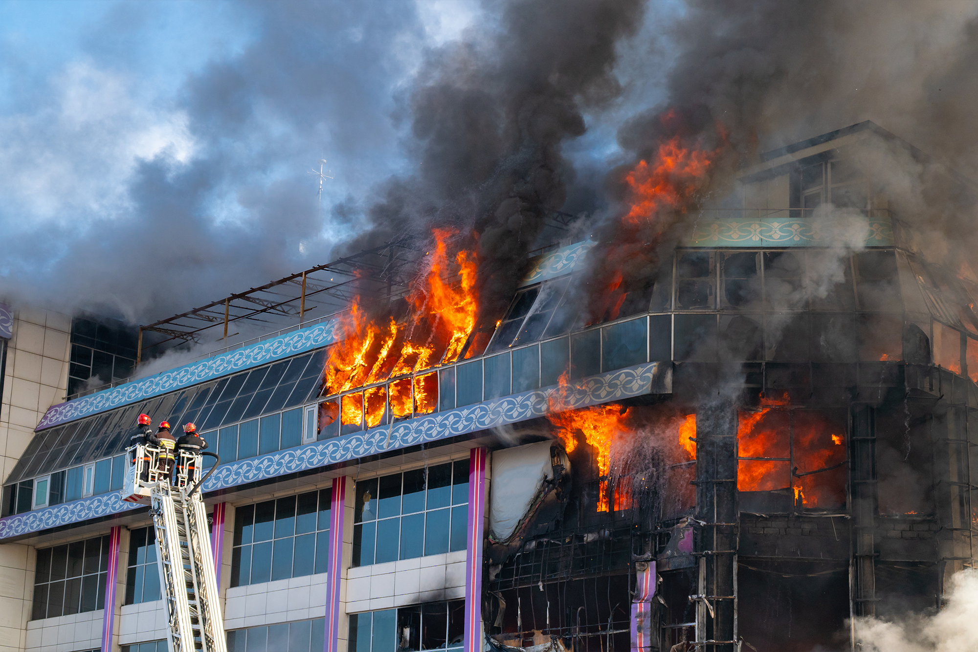 A building on fire with firefighters on a ladder trying to extinguish the disaster. 