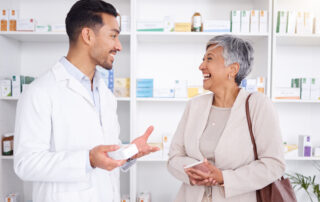 4 Key Trends Driving Employer Healthcare Costs in 2024: Pharmacist man, senior woman and talking with box, phone or funny in store for prescription, health or help. Young pharmacy manager, elderly patient and comic chat for care with customer experience.