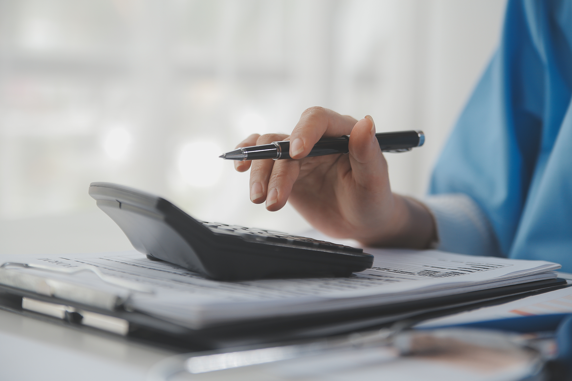 IRS Raises 2024 Health FSA Cap. A person with a pen in their hand using a calculator.
