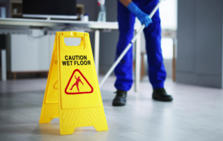 5 Tips for Preventing Slips, Trips, and Falls on School Premises: A janitor cleaning up a classroom with a mop. There is a Caution Wet Floor sign in the foreground.