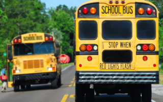 Safeguarding School Transportation - Two school buses facing opposite directions, with the stop lights flashing.