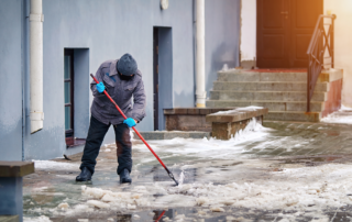 De-icing Outdoor Walking Surfaces in Winter: A man clearing off a sidewalk in winter.