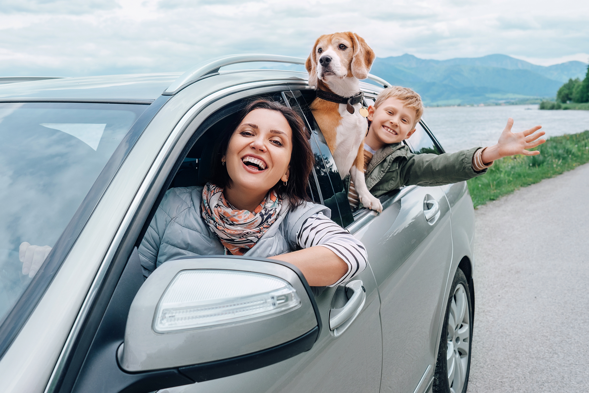 Tips for Auto Insurance Buyers in 2024: A mother in the driver's seat of a sedan with her young child and pet dog looking out the passenger window.