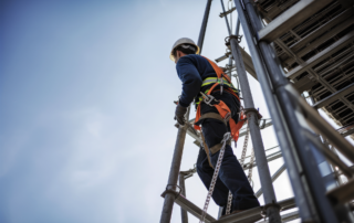 Housekeeping and Ladder Safety: A construction worker using protective fall gear on a ladder.