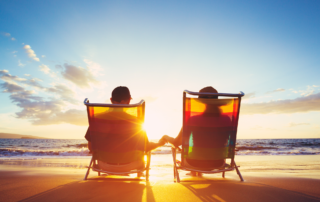 SECURE 2.0 Means Major Retirement Changes in 2024: A retired couple sitting on the beach facing the sunset over the water.