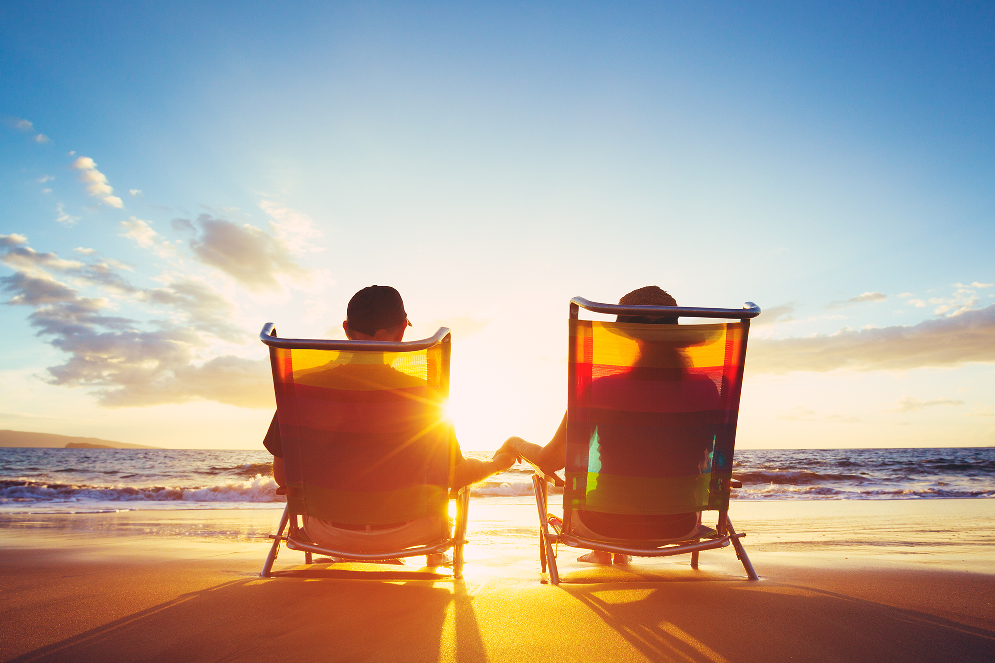 SECURE 2.0 Means Major Retirement Changes in 2024: A retired couple sitting on the beach facing the sunset over the water.