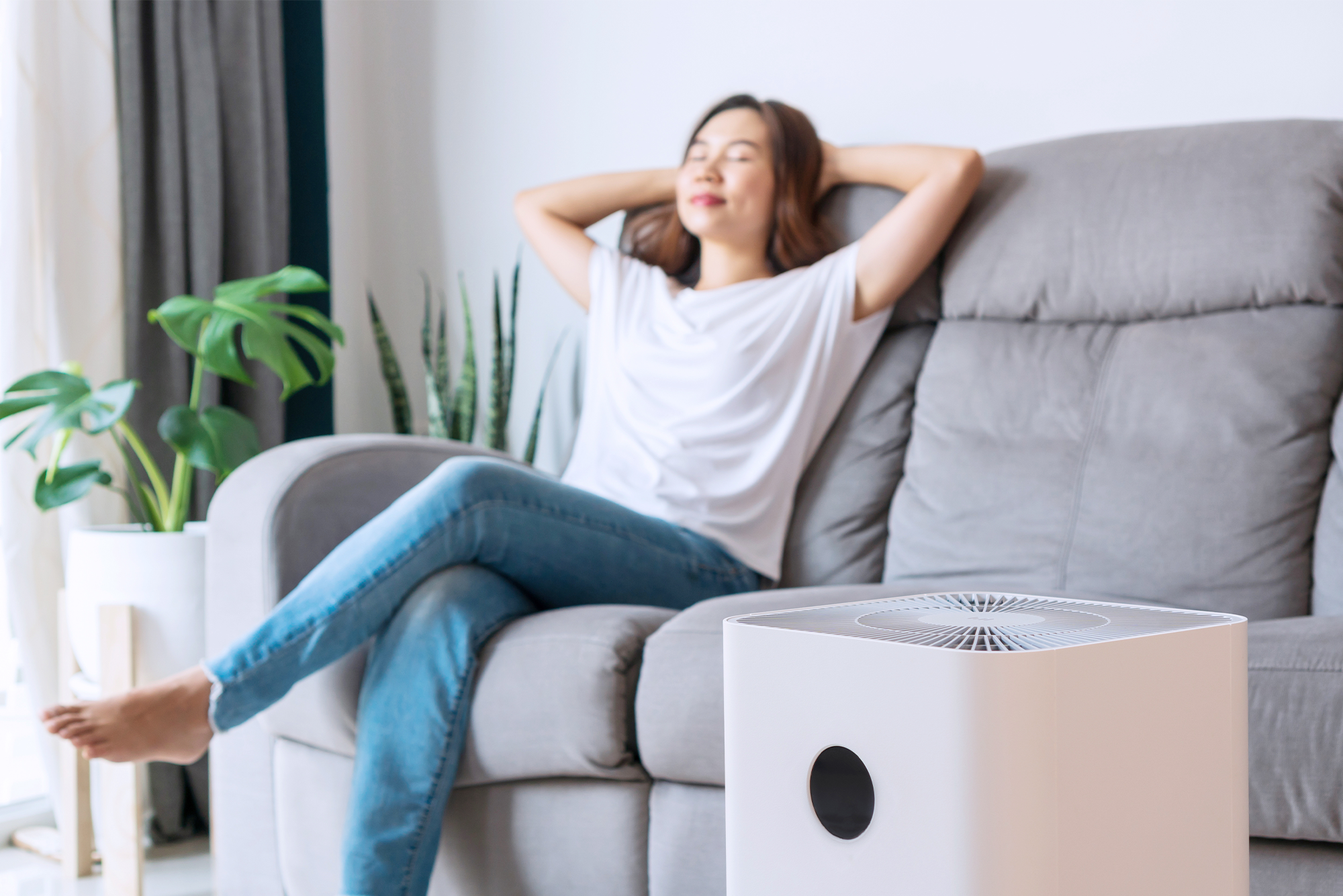 Eliminating Indoor Air Pollution: A female sitting on her couch with an air purifier in the foreground.