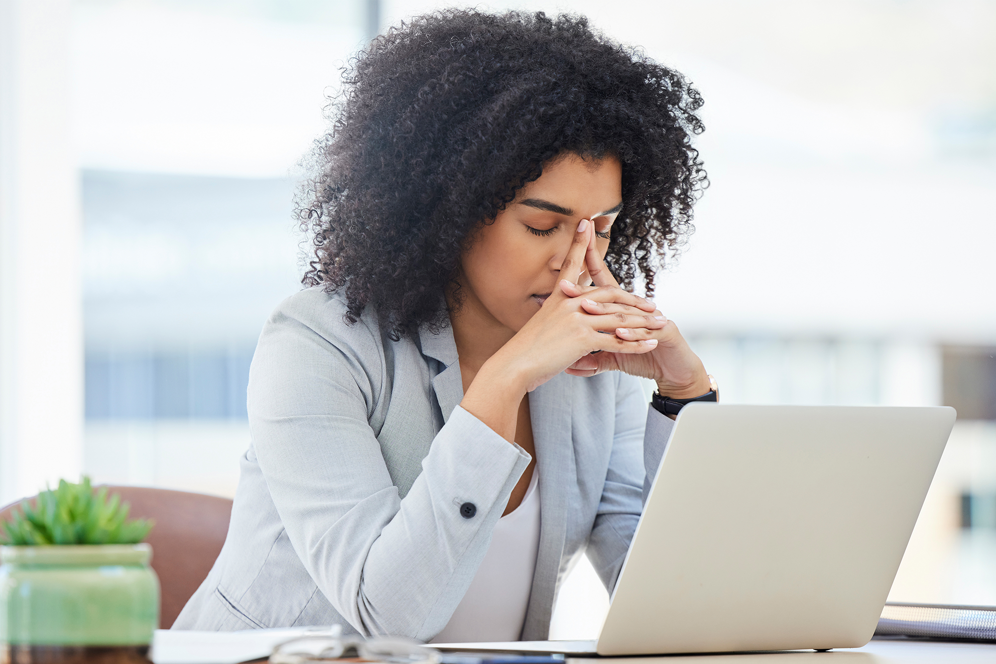 Supporting Employees During Mental Health Awareness Month and Beyond: A stressed out female colleague sitting at her desk with her head in her hands.