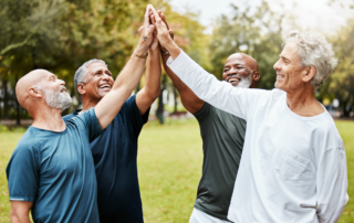 How Targeted Wellness Programs Can Reduce Workers' Compensation Claims: A group of men high-fiving in the park.