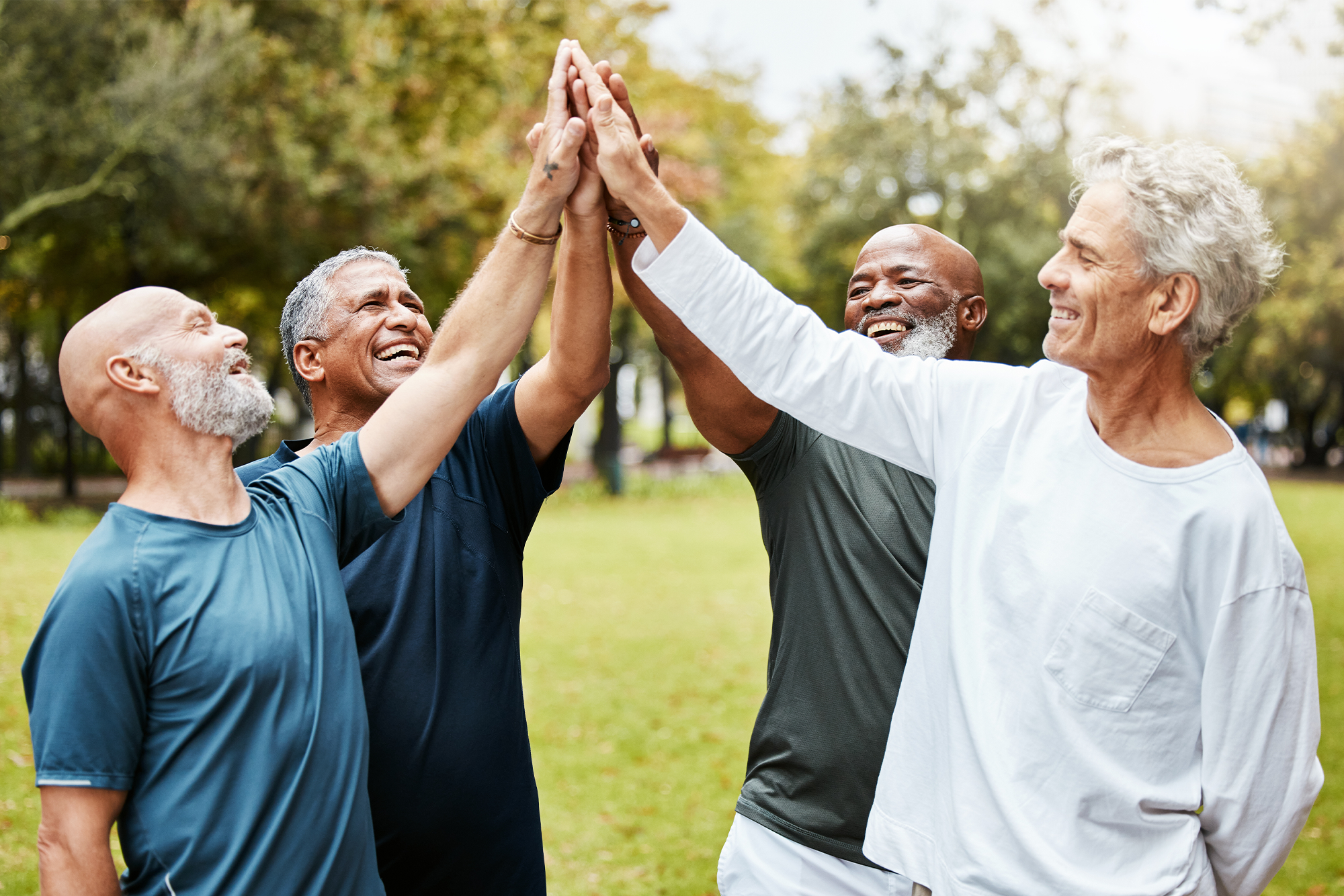 How Targeted Wellness Programs Can Reduce Workers' Compensation Claims: A group of men high-fiving in the park.