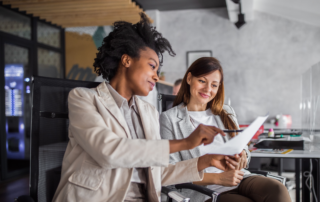 Getting the Most Out of Your 2025 Open Enrollment Communications: two female colleagues discussing their open enrollment options