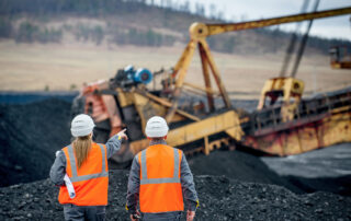 Monitoring to Prevent Patterns of Violations: two mine workers in orange safety vest overlooking a coal operation.