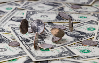 US currency laid out on a table with coins falling on top. Compensation growth slowed slightly in the third quarter of the year, signaling that the white-hot labor market is cooling off.