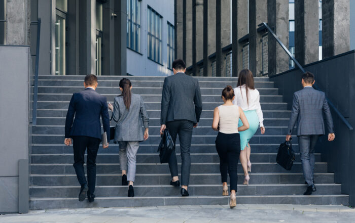 Rear view of Six Business People Walking up the Stairs. Men and women in formal suits going up stairs into office building. Partnership, communication business people concept.